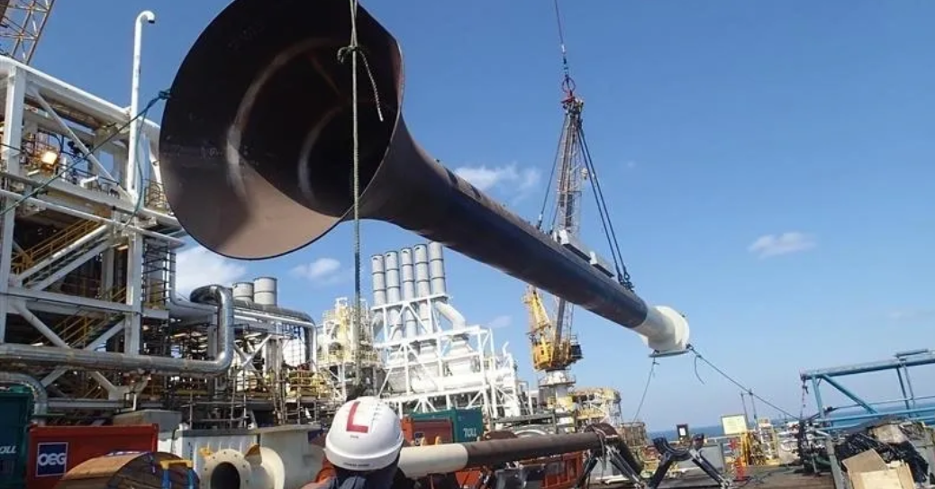 Crane lifting a large pipe spool into position on an offshore platform