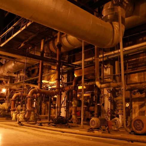 Pipework, pumps and valves running through a floodlit industrial plant room