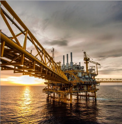 Offshore oil and gas production platform with pipe bridge at sunset